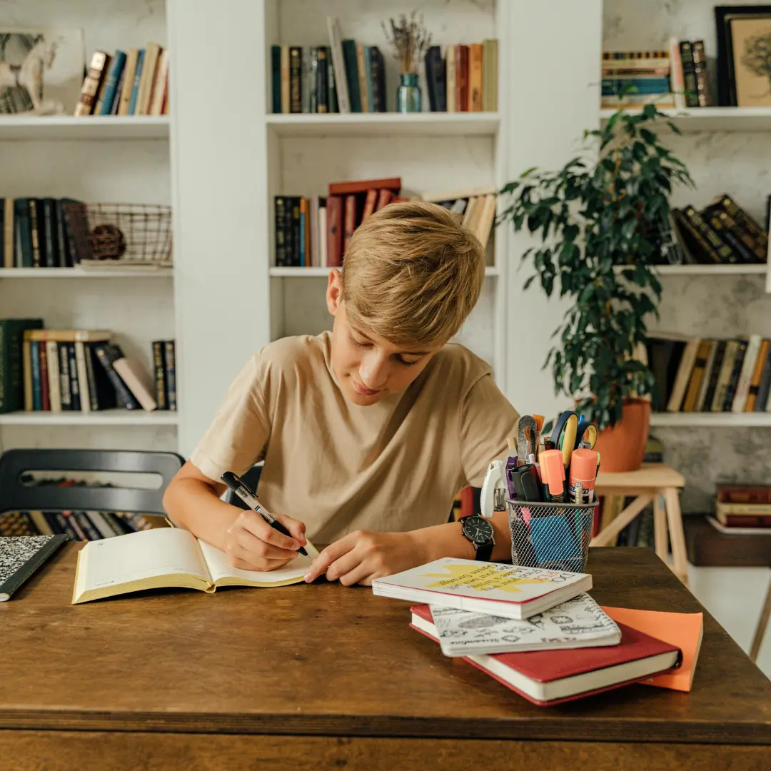 Un ragazzo che scrive in un quaderno mentre studia a casa.