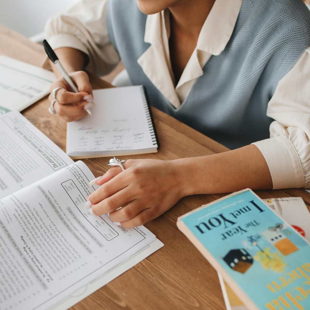 Studente che prende appunti su un quaderno mentre legge un libro.